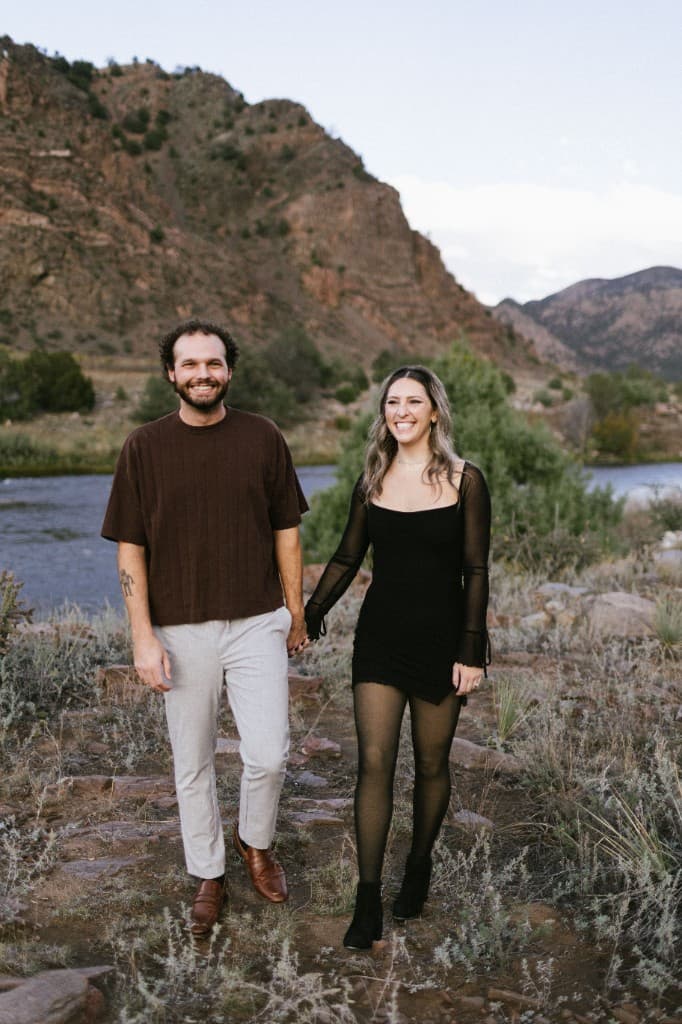 Riley and Canon standing together by a river, holding hands